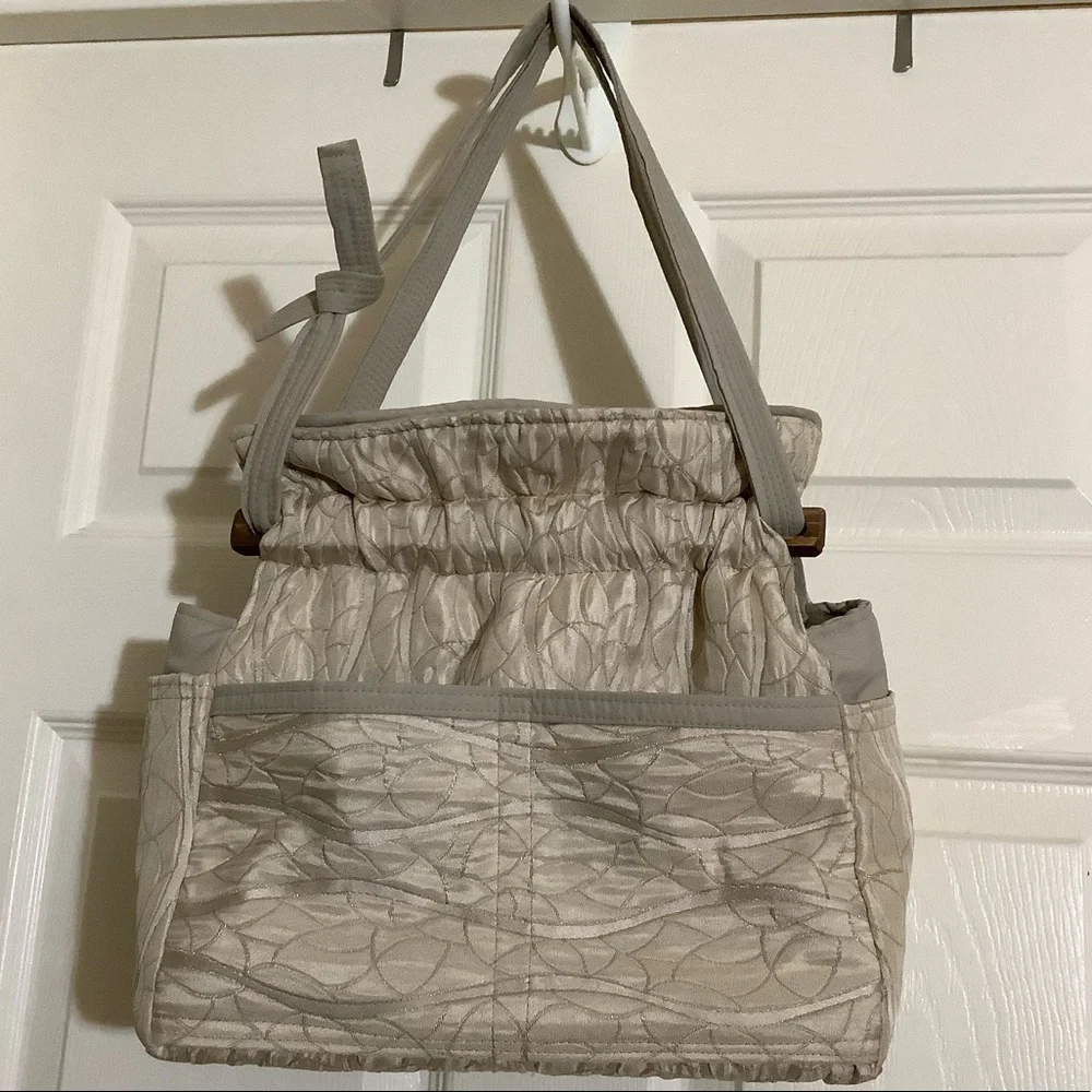 FABRIC SHOULDER BAG WITH OUTSIDE SURROUNDING POCKETS IN A CREAM AND TAUPE COLOR.